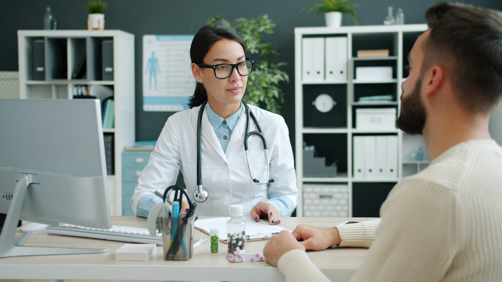 A clinician talks with a patient across the desk in a clinic room